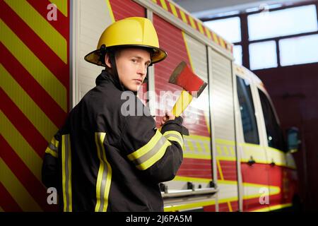 Pompiere completamente equipaggiato con casco e ascia in fondo camion antincendio. Foto Stock