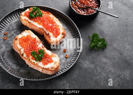 Due dandwiches con caviale rosso. Caviale rosso salmone in ciotola e sandwich server su vecchio piatto di ferro su sfondo vecchio tavolo nero. Vista dall'alto. Spazio di copia. Foto Stock