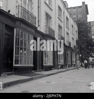 1960s, Historical, Woburn Walk, Bloomsbury, Londra, Inghilterra, Regno Unito. Nella foto sono visibili il servizio Valet di Woburn e Helena Gee. Una strada pedonale per lo shopping, il suo nome deriva da Woburn Abbey, la sede inglese dei Duchi di Bedford, che possedevano e sviluppavano l'area. Progettato da Thomas Cubitt nel 1822, è stata la prima strada pedonale di Londra costruita appositamente per lo shopping. Le facciate del negozio hanno un aspetto distintivo, con le finestre costituite da piccole singole lastre di vetro e di essere Dickensian fiocco-fronted in stile. Foto Stock