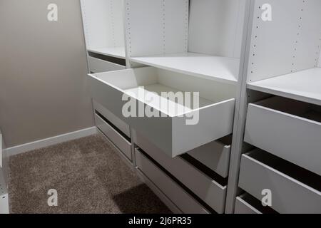 Vista di alti armadi e cassetti bianchi all'interno di una stretta passeggiata in armadio all'interno di una camera da letto principale Foto Stock