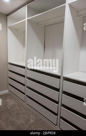 Vista di alti armadi e cassetti bianchi all'interno di una stretta passeggiata in armadio all'interno di una camera da letto principale Foto Stock