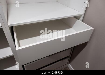 Vista di alti armadi e cassetti bianchi all'interno di una stretta passeggiata in armadio all'interno di una camera da letto principale Foto Stock