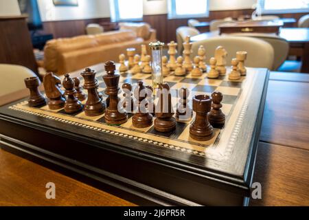 Vista ad angolo di una bella scacchiera in legno, con pezzi di legno chiaro e scuro, sulla cima di un tavolo da pranzo in legno scuro Foto Stock