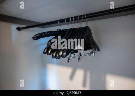 Vista ad angolo di grucce in legno nero con clip all'interno di un pulito armadio bianco della camera d'albergo Foto Stock