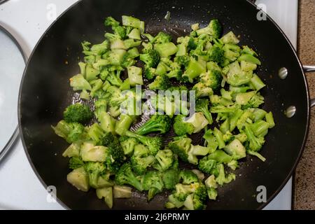 Vista dall'alto di broccoli surgelati tritati in una padella nera su un piano di cottura bianco Foto Stock