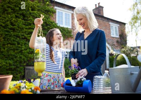 Madre e figlia che fanno i supporti riciclati dell'impianto dai rifiuti di imballaggio della bottiglia di plastica nel giardino a casa Foto Stock