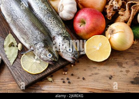 Due trote arcobaleno su tavola in legno rustico tra erbe e verdure. Cibo sano Foto Stock