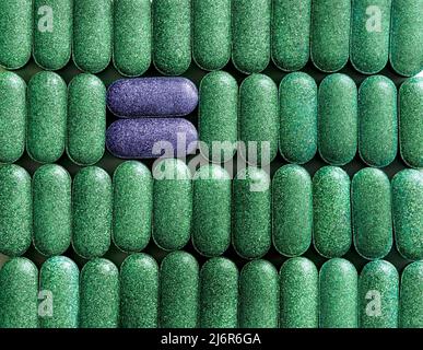 Clorella, spirulina o erba d'orzo in fila a forma di pillola e due pillole viola attraverso primo piano sfondo nutrizionale supplemento, detox superfood healt Foto Stock
