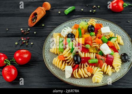 Penne pasta con verdure, piselli, peperoni dolci, pomodori, salsa, mozzarella su sfondo di legno nero. Pasta italiana con verdure e sp Foto Stock