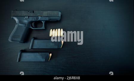 Pistola con due scomparti e munizioni da 9 mm su tavolo in legno nero con spazio di copia, sfondo scuro Foto Stock
