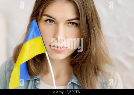 La ragazza seria indipendente tiene la bandiera Ucraina e gli occhi vicini. Patriot del suo paese. Prega per l'Ucraina. Lotta per la libertà. Stop guerra. Blu giallo. Foto Stock