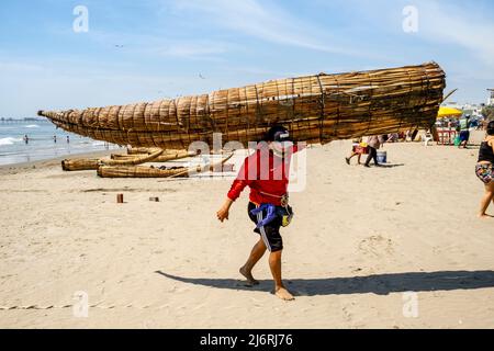 Un pescatore che porta un Caballito de Totoro (tradizionale barca a vela), Spiaggia di Pimentel, Chiclayo, Provincia di Chiclayo, Perù. Foto Stock