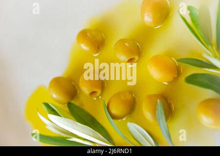 Olive e olio d'oliva. Olive verdi e ramo d'oliva in olio d'oliva in un piatto grigio primo piano .olio naturale spremuto a freddo Foto Stock