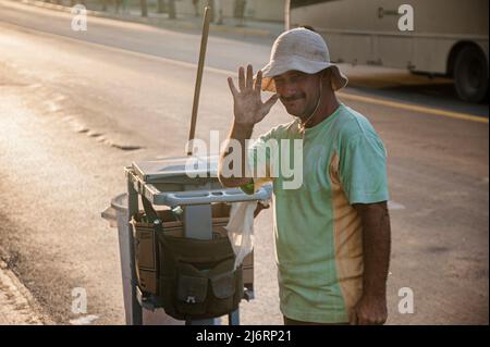 Il pulitore di strada cubano sorride e ondeggia alla macchina fotografica durante il tramonto del cielo di colore arancione a Varadero, Cuba. Foto Stock