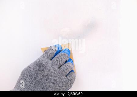 Un uomo pulisce la vecchia vernice su una porta di legno con carta vetrata. Smussatura delle irregolarità. Foto Stock