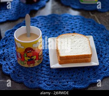 colazione su un tavolo di granito con un piatto quadrato bianco e una tazza colorata di latte, fette di pane con burro di arachidi Foto Stock