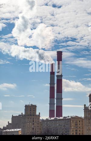 CHP in città. Il fumo sale nel cielo dai tubi di calore della centrale elettrica. Tubo di centrale combinata di calore e di potenza CHP o cogenerazione contro ba Foto Stock