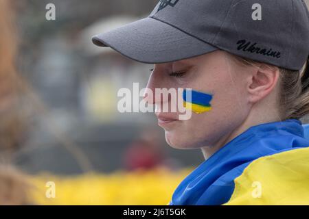 Una giovane donna con una bandiera dell'Ucraina dipinta sulla sua guancia visto piangere durante la manifestazione. Mogli, madri, bambini di soldati ucraini e membri del Battaglione Azov a Mariupol si sono riuniti nella piazza dell'Indipendenza per chiedere ai leader mondiali di contribuire a organizzare un corridoio umanitario per l'evacuazione di civili e militari ucraini dalla città assediata di Mariupol ai paesi neutrali. Foto Stock