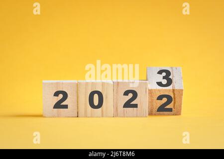 Legno cubo di flipping stock, cambiare da 2022 a 2023. Sfondo giallo, con spazio di copia. Foto Stock