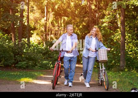 Concetto attivo di vecchiaia, gente e lifestyle felice coppia senior in bicicletta nel parco estivo in una giornata di sole in abiti casual confortevole, godere la vita e il tempo trascorso insieme Foto Stock