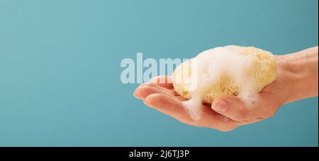 Mano di persona anonima che mostra una spugna con schiuma su sfondo turchese Foto Stock