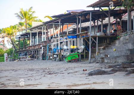 Vista di edifici in legno sul fronte spiaggia a Batu Bolong Beach a Canggu, Bali con persone sedute. Foto Stock