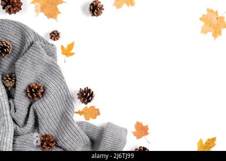 Spazio di lavoro con foglie d'acero dorato, coni, maglione grigio sulla parete bianca dello studio. Composizione creativa. Concetto di autunno o inverno. Disposizione piatta Foto Stock