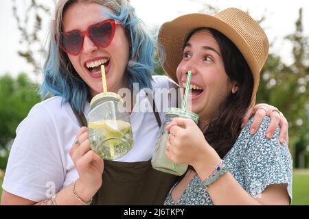 Due amiche felici che bevono bevande rinfrescanti, ridono e abbracciano. Foto Stock