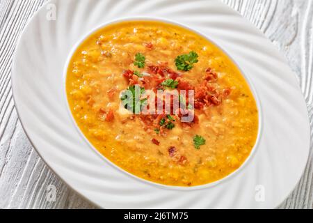 zuppa di mais cremosa con pancetta fritta croccante sbriciolata e prezzemolo in ciotola bianca su tavola di legno bianco, primo piano Foto Stock