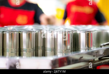 Molte lattine su lavoratori di sfocatura. Fabbrica di pesce in scatola. Industria alimentare. Lavoratori che lavorano in fabbriche di alimenti in scatola per riempire sardine in lattine. Cibo Foto Stock