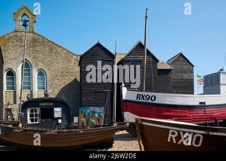 Barche e capannoni di rete sullo Stade, Hastings Old Town, East Sussex UK, con il Museo dei pescatori ospitato in una ex chiesa Foto Stock