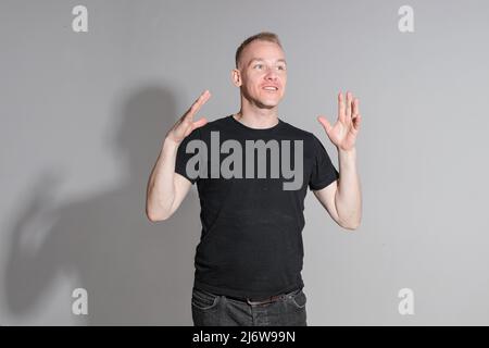 Vivace uomo caucasico in camicia nera in posa su sfondo grigio Foto Stock