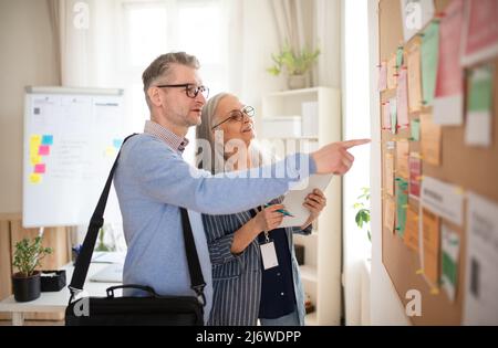 Dipendente dell'agenzia di reclutamento che si trova di fronte alla bacheca del lavoro e aiuta l'uomo maturo a cercare un lavoro. Foto Stock