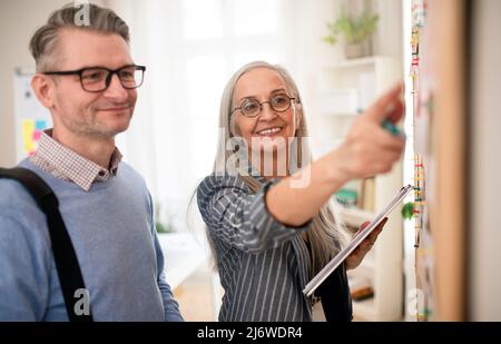 Dipendente dell'agenzia di reclutamento che si trova di fronte alla bacheca del lavoro e aiuta l'uomo maturo a cercare un lavoro. Foto Stock