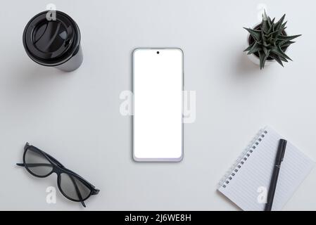 Telefono grigio sulla scrivania. Schermo isolato per la presentazione del design dell'app. Vista dall'alto, composizione piatta con tazza da caffè, bicchieri, cialda, penna e pla Foto Stock