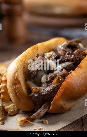 Primo piano di sandwich di cheesesteak philly fatto con bistecca, formaggio e cipolle su un rotolo di hoagie tostato con patatine fritte su un tavolo di legno Foto Stock