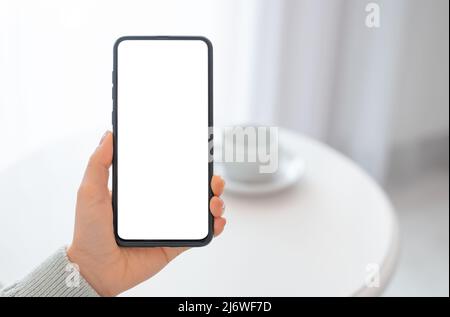 Mockup immagine donna che tiene nero cellulare con schermo vuoto con caffè sul tavolo. Mano donna che tiene cellulare con schermo vuoto scrivania. Da a. Foto Stock