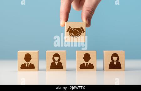 contratto commerciale. Mano che mette la mano scuotendo sul blocco di legno del cubo di fronte all'icona umana per affare di affari e concetto di accordo. Comunicazioni aziendali Foto Stock