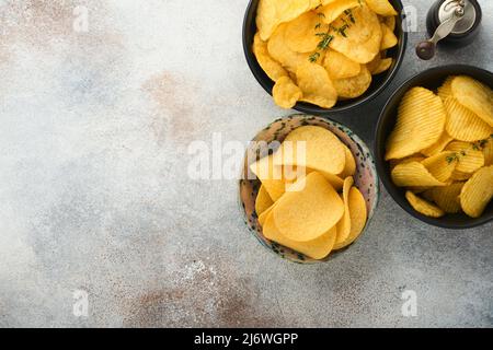 Spuntini. Cibo malsano. Tutti i classici spuntini di patate con arachidi, anelli di popcorn e cipolle e pretzel salati in ciotole su fondo grigio di cemento Foto Stock