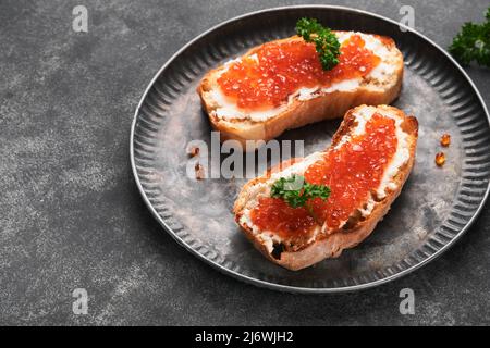 Due dandwiches con caviale rosso. Caviale rosso salmone in ciotola e sandwich server su vecchio piatto di ferro su sfondo vecchio tavolo nero. Vista dall'alto. Spazio di copia. Foto Stock