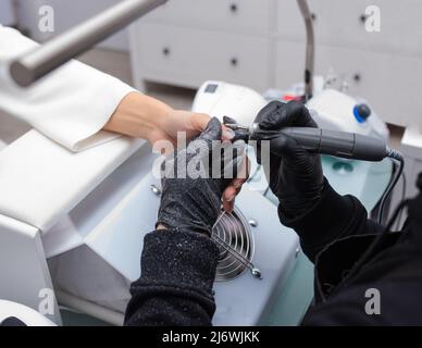 Il manicurista rimuove lo smalto per unghie utilizza la macchina elettrica della lima per unghie durante la manicure. Foto Stock