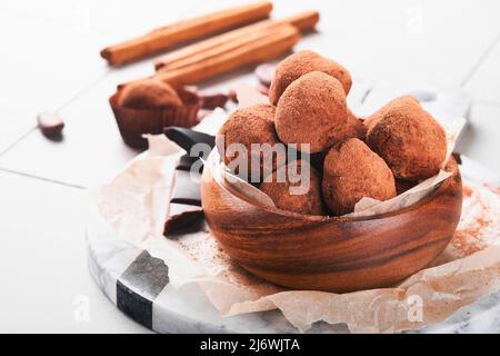 Tartufi di cioccolato con polvere di cacao in piatto di legno su vecchio sfondo di piastrelle cracked tavolo. Gustose caramelle dolci al tartufo di cioccolato. San Valentino e. Foto Stock