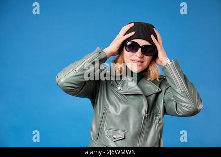 Ragazza gioiosa con cappuccio nero tiene le mani in testa, ha un sorriso divertente, indossando una giacca verde Foto Stock