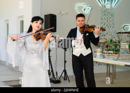 Un uomo in un cappotto di coda e una donna in un abito da sera giocare il violino. Duo di violinisti. Foto Stock