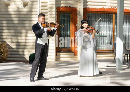 Duo di violinisti. Un uomo in un cappotto di coda e una donna in un abito da sera giocare il violino. Foto Stock