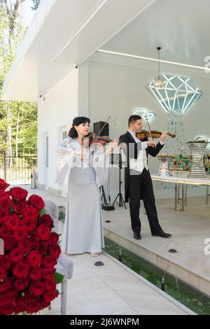 Un uomo in un cappotto di coda e una donna in un abito da sera giocare il violino. Duo di violinisti. Foto Stock