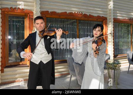 Duo di violinisti. Un uomo in un cappotto di coda e una donna in un abito da sera giocare il violino. Foto Stock