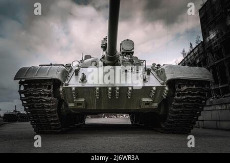 vecchio carro armato sovietico sullo sfondo di case distrutte. Il concetto di guerra in Europa. L'offensiva di pesanti veicoli corazzati per le strade della città Foto Stock