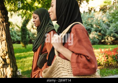 Donne musulmane multirazziali vestite in hijabs che parlano durante camminare al parco verde Foto Stock