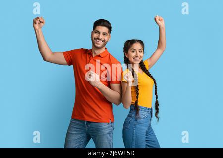 Grande successo. Ritratto di giovane coppia araba gioiosa che alza i Fists con l'eccitazione Foto Stock